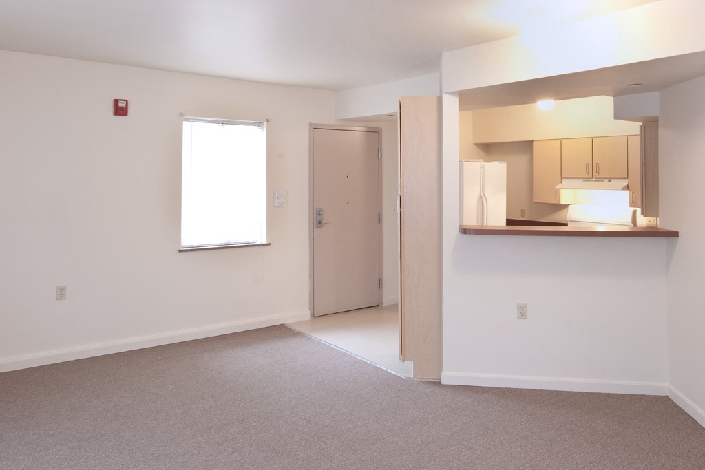 an empty living room with a kitchen and a window