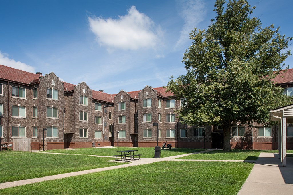 a large brick apartment building with a picnic table in the courtyard