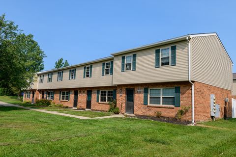 an apartment building with brick and tan siding and green grass