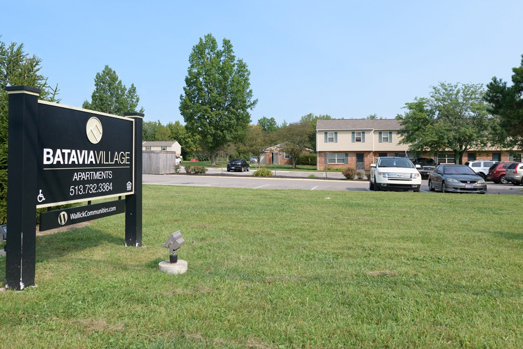 a sign sits in the grass in front of a parking lot