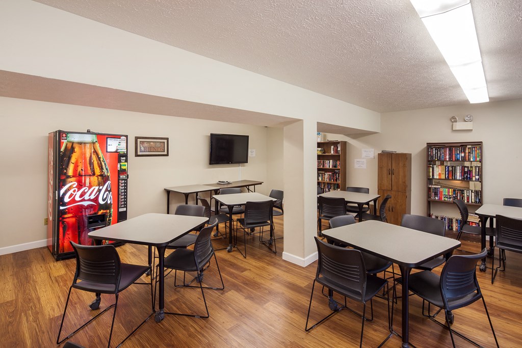 a common area with tables and chairs and a coke machine