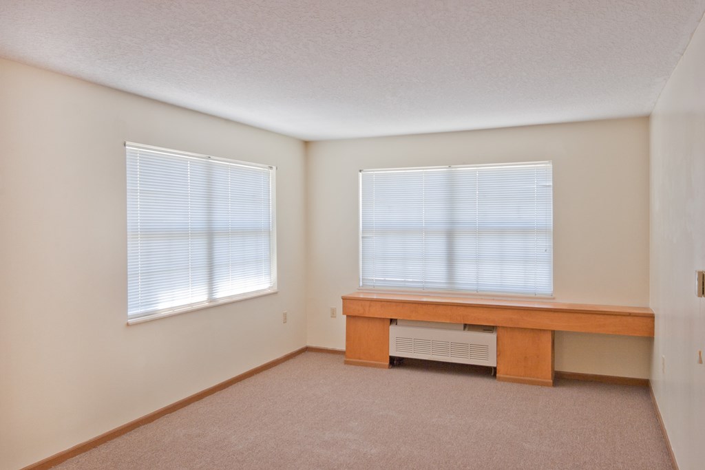 a living room with a desk and two windows