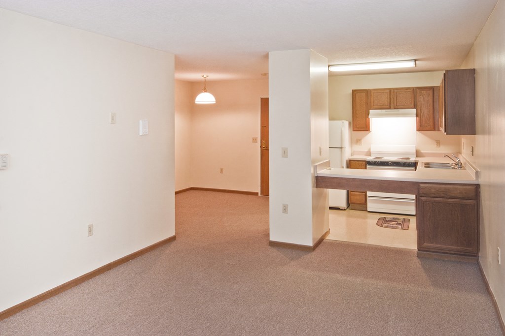 an empty living room with a kitchen and an open doorway