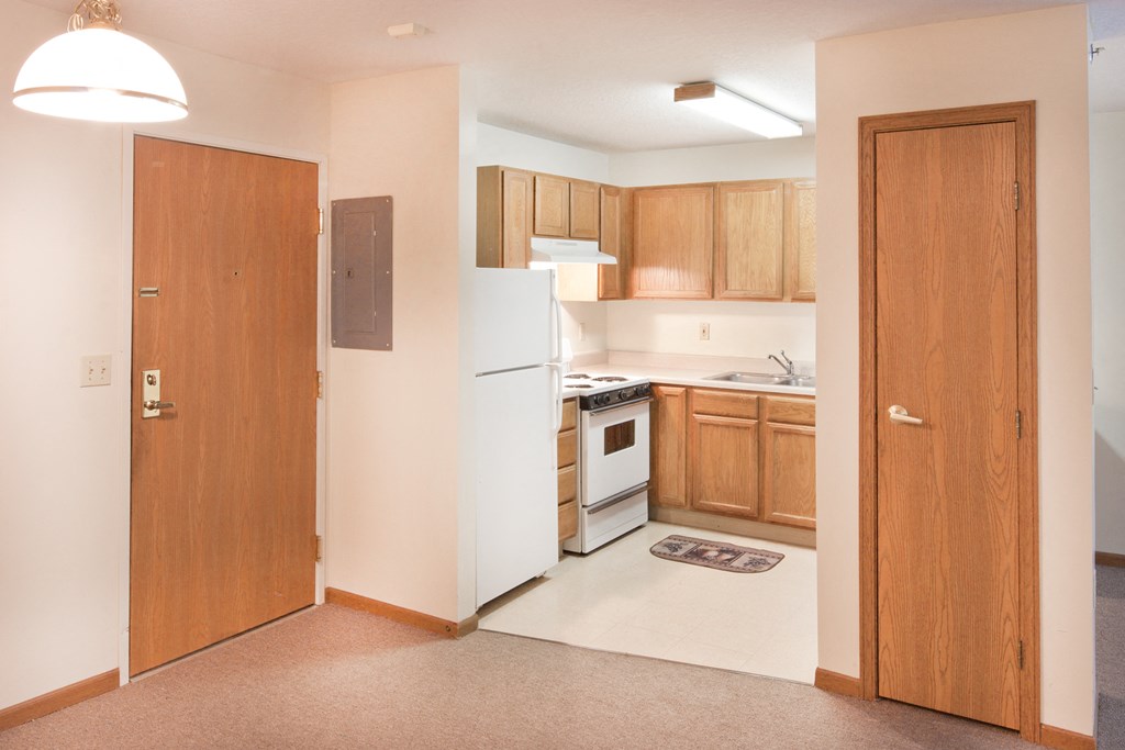 an empty kitchen with a white refrigerator and a door to the kitchen