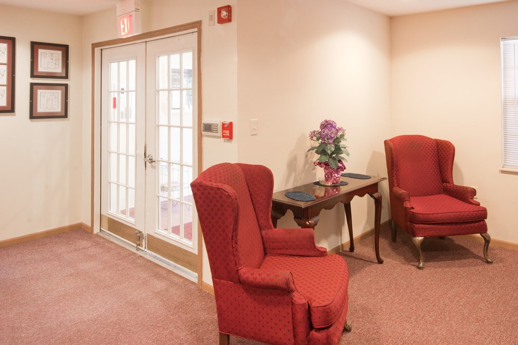 a waiting room with two red chairs and a table with flowers