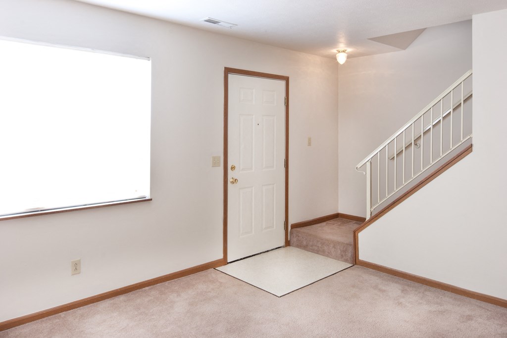 an empty living room with a white door and a stairwell