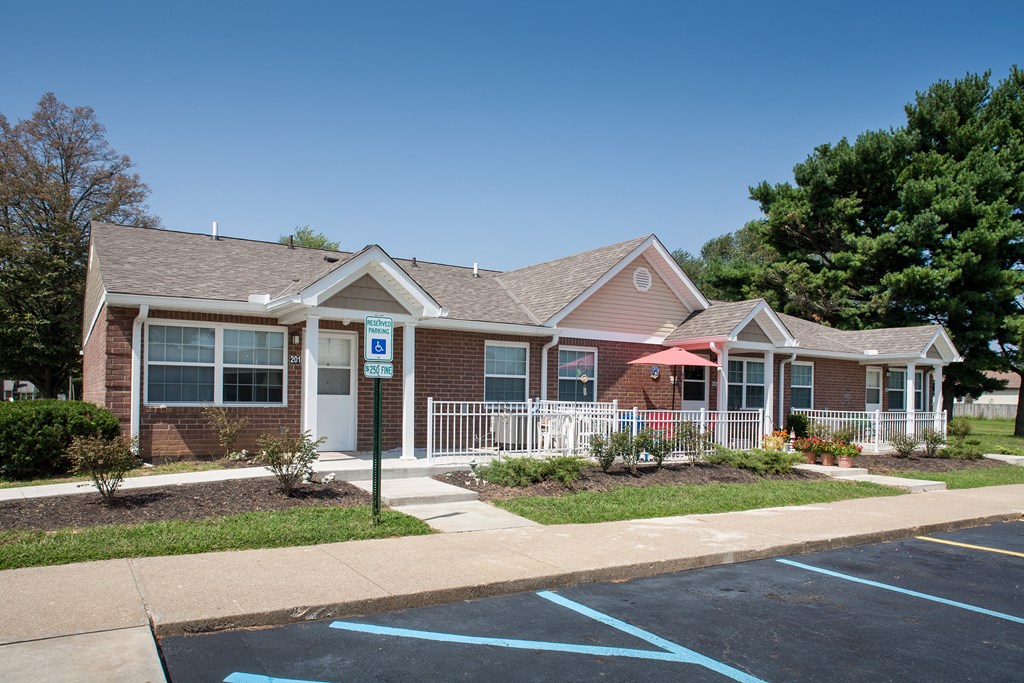 a brick house with a porch and a sidewalk in front of a parking lot
