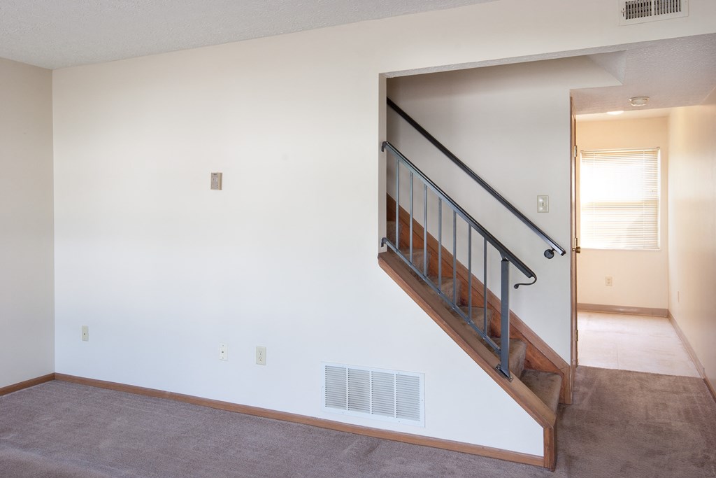 a living room with a staircase and a white wall and a door to a hallway