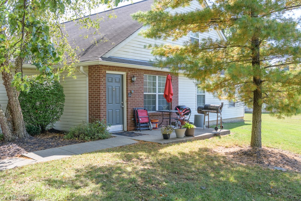 a front porch of a home with a grill and a tree