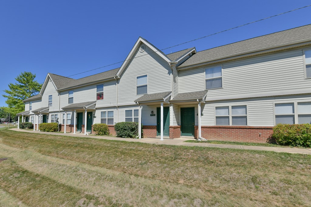 a row of white houses with green doors and a grass field