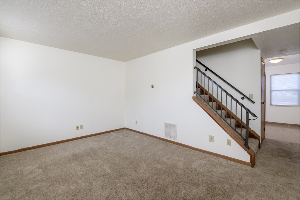 the living room and dining room of an empty home with carpeting and a staircase