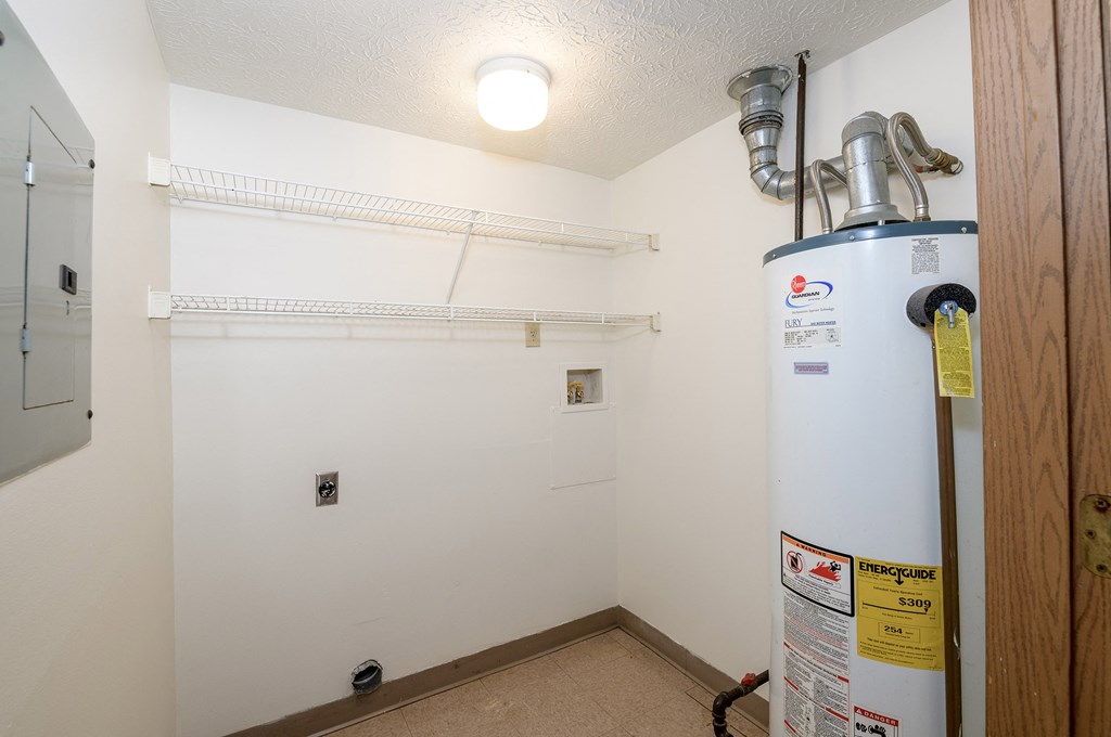 a room with a water heater in the corner and a white wall with a closet