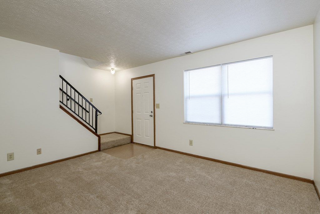 the living room and entryway of a small house with a large window and carpet