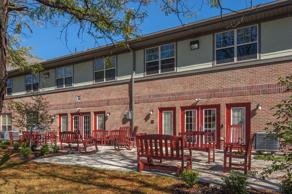 a patio with benches and chairs in front of a brick building