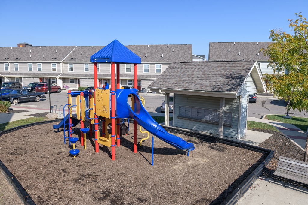 a playground with a blue and red swing set in front of a building