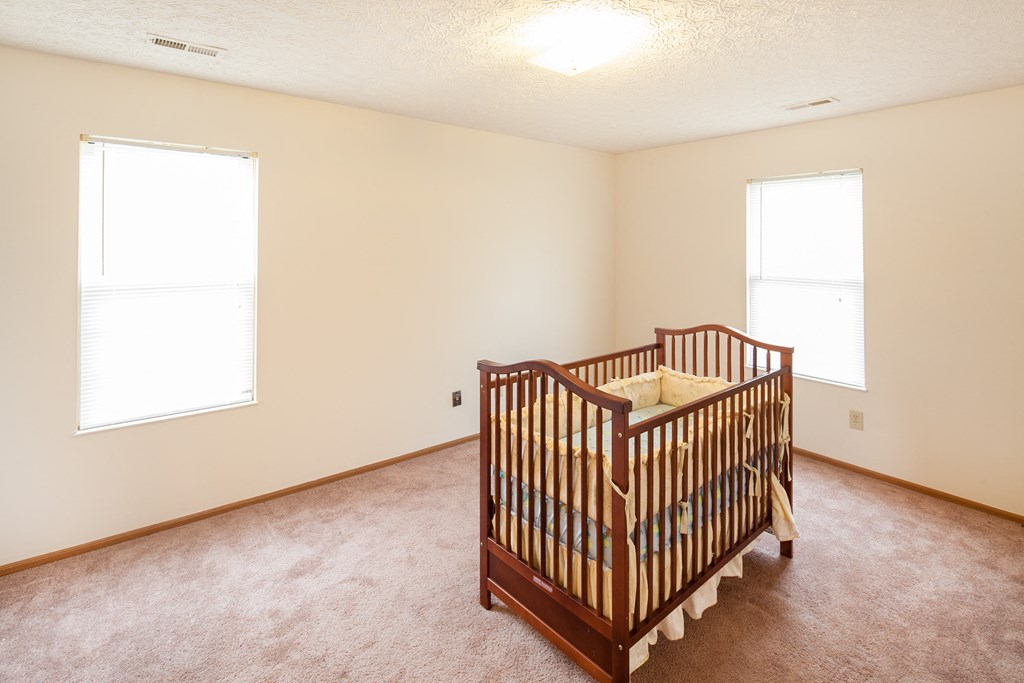 a nursery with a crib in a room with carpet and two windows
