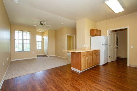 an empty living room with a kitchen and a refrigerator