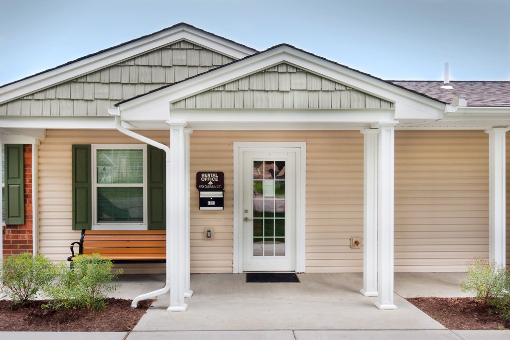 the front entrance of a small yellow house with a bench
