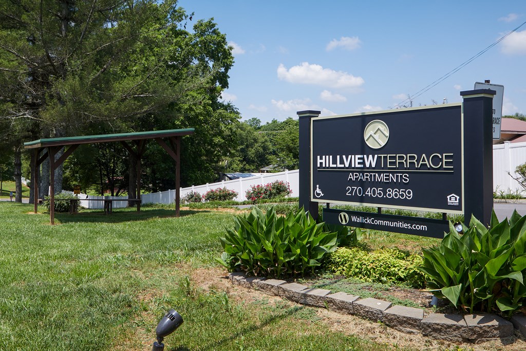 a sign for hillside terrace apartments in front of a garden with a sign