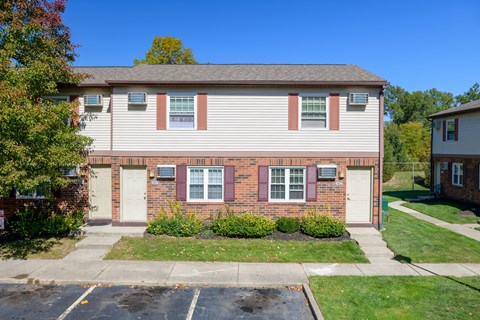 a brick house with white siding and pink shutters and a lawn