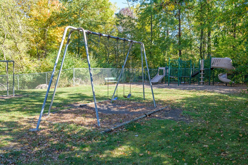 a swing set in a park with trees and a fence