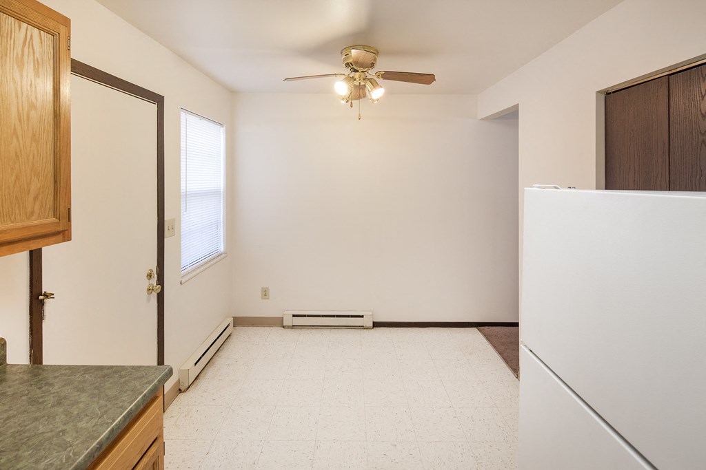 an empty kitchen with a refrigerator and a ceiling fan