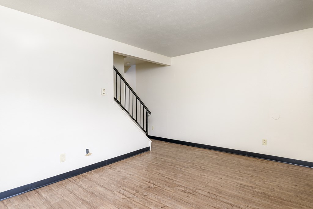 an empty living room with white walls and wood flooring and a staircase