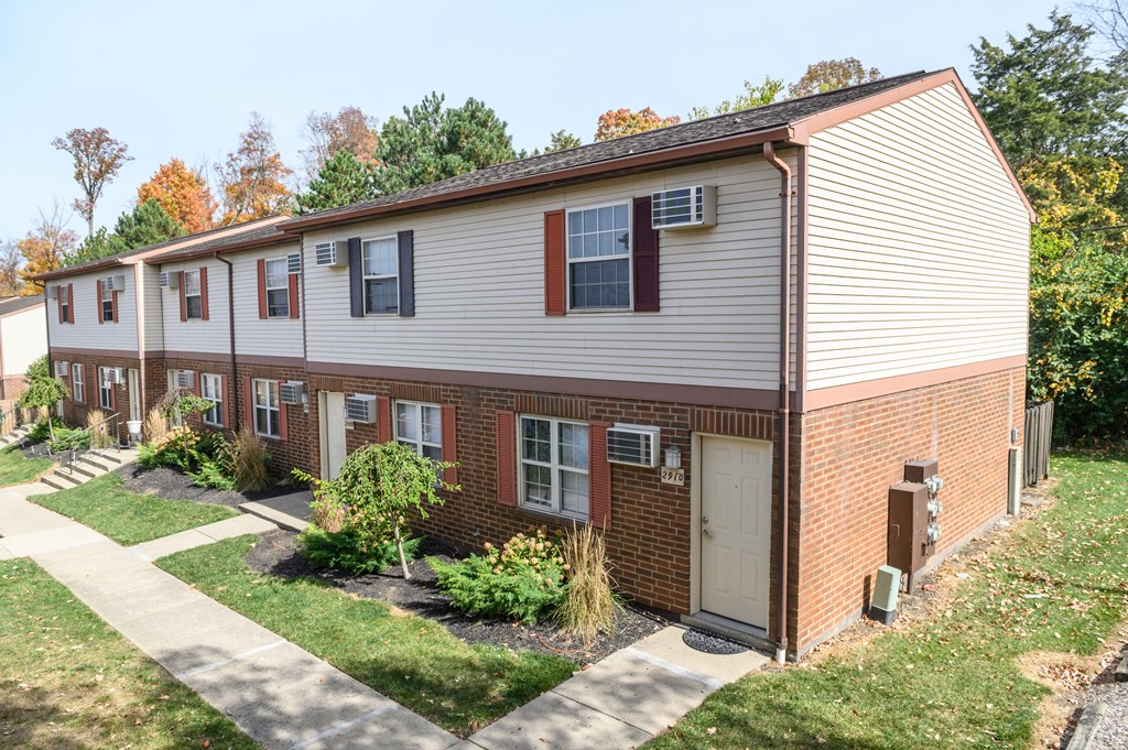 a white and brick apartment building with a sidewalk and grass