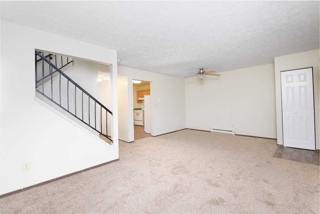 an empty living room with white walls and a white door and a staircase