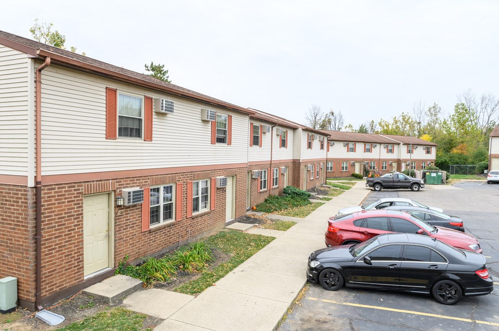 a row of apartment buildings with cars parked in a parking lot