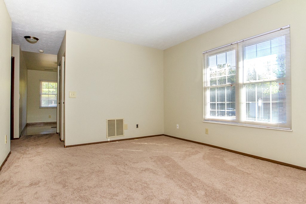 the spacious living room of an empty home with a large window