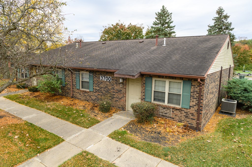 a small brick house with green shutters and a sidewalk