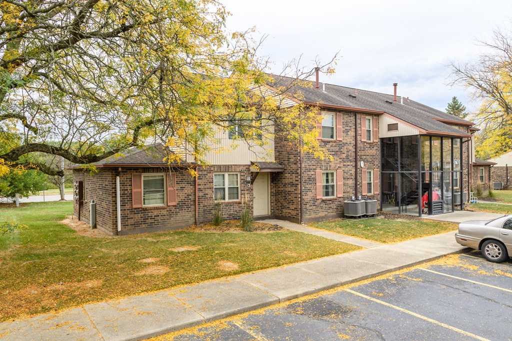 the front of a brick house with a driveway and a tree