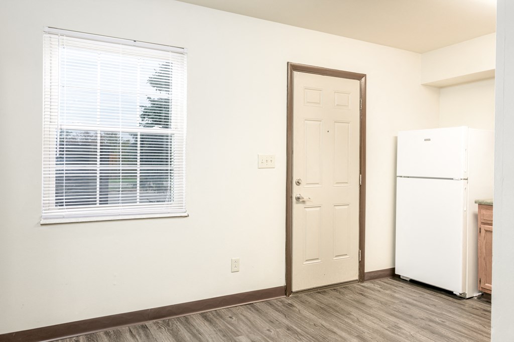 an empty room with a refrigerator and a window and a door