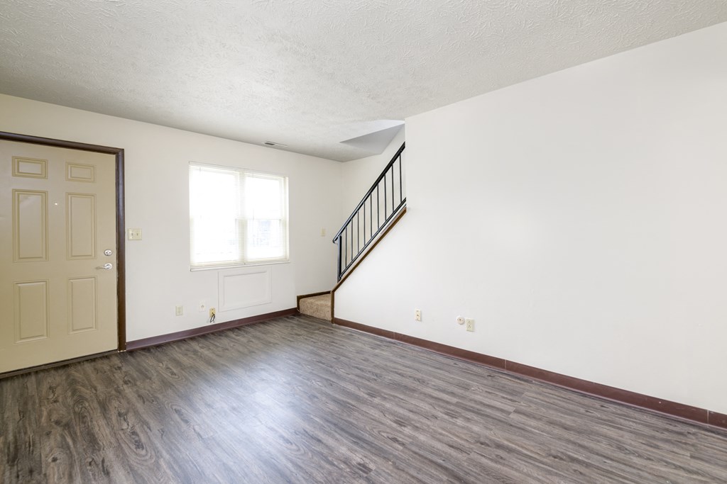 an empty living room with white walls and wood floors and a door