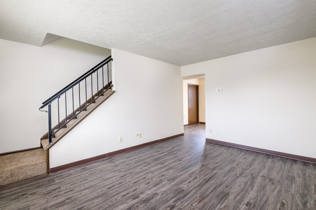 an empty living room with white walls and wood flooring and a staircase