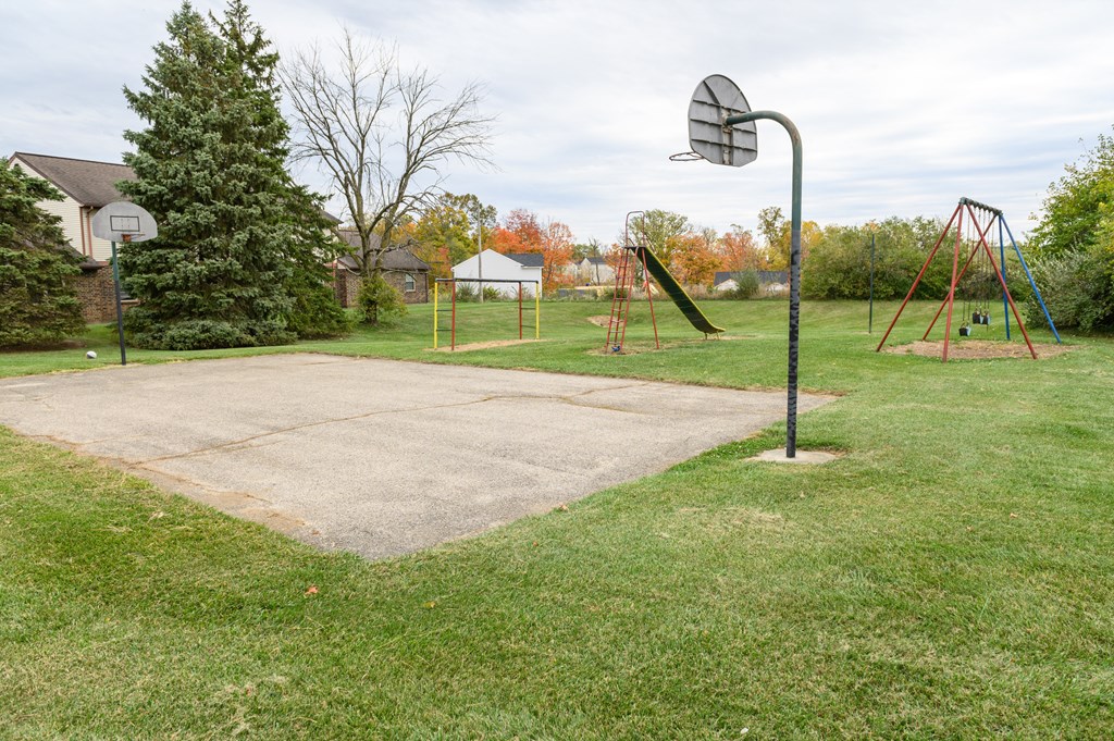 a basketball court with a swing set and a basketball hoop on the grass
