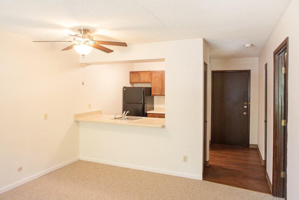an empty living room with a kitchen and a ceiling fan