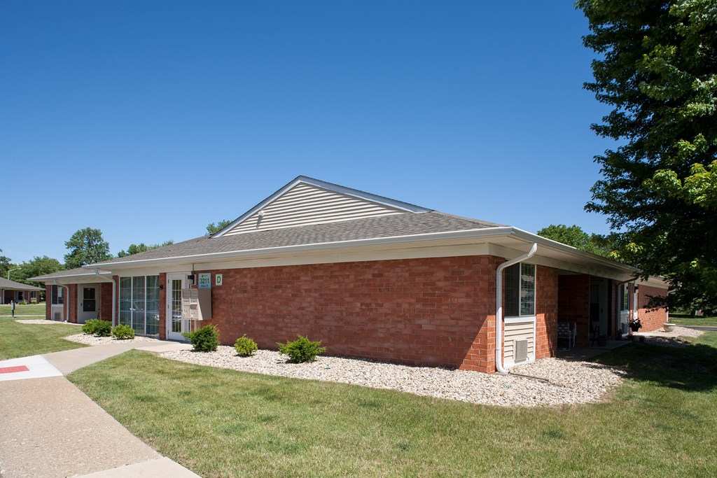 the front of a brick building with grass and trees