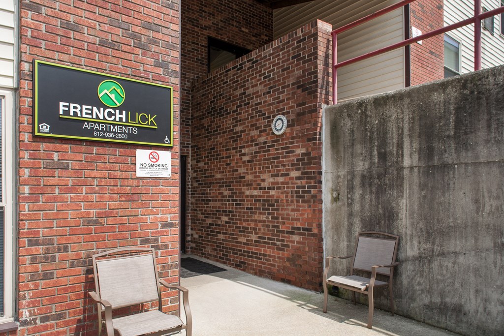 two chairs in front of a brick building with a lick apartments sign