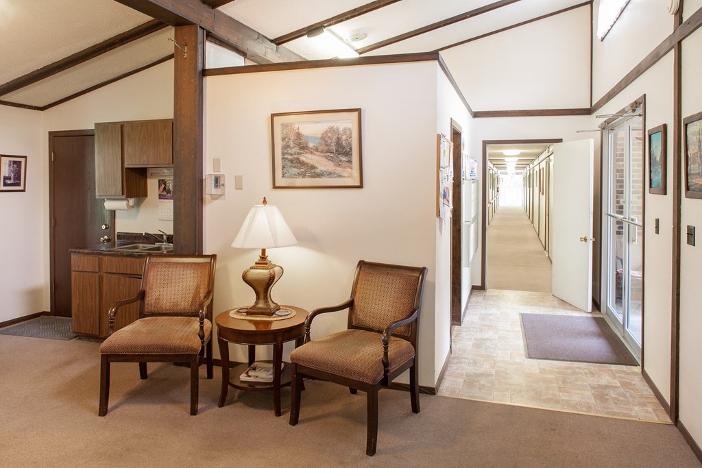 a hallway with two chairs and a table with a lamp   and a kitchen