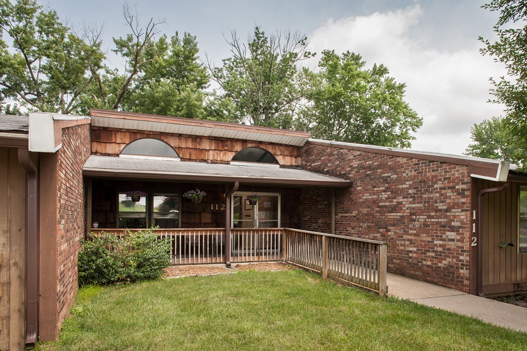 the front of a brick building with a porch and a lawn