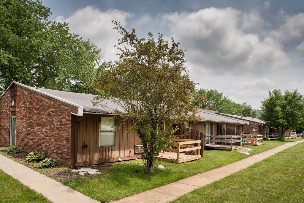 a small brown house with a porch and a tree in front of it