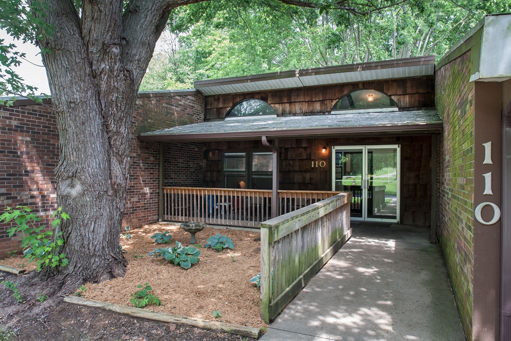the front of a brick building with a porch and a tree