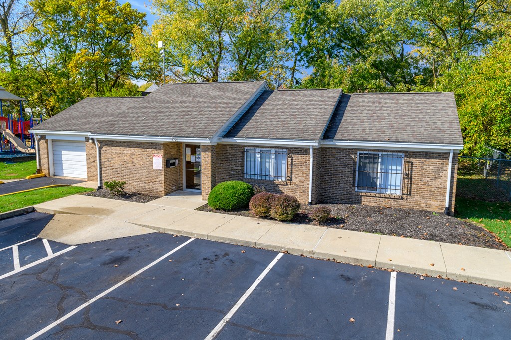 the front of a brick house with a parking lot and trees