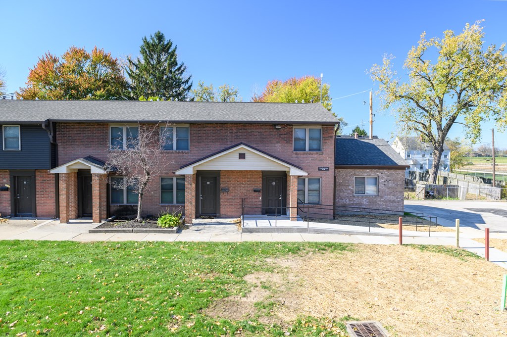 the front of a brick house with a yard and a sidewalk