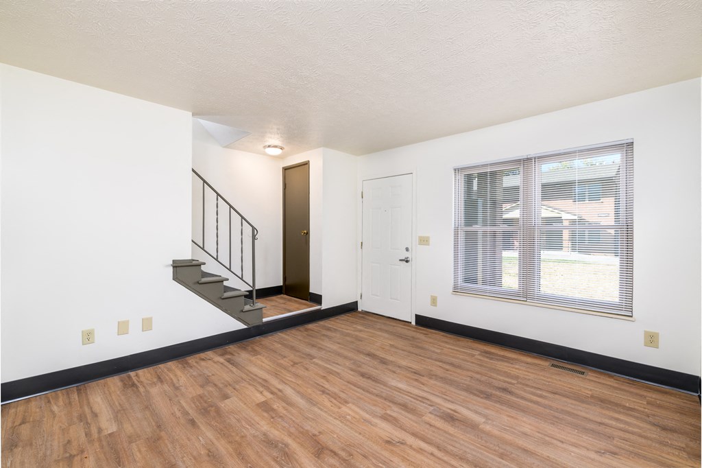 the living room and entryway of an apartment with wood flooring and a window