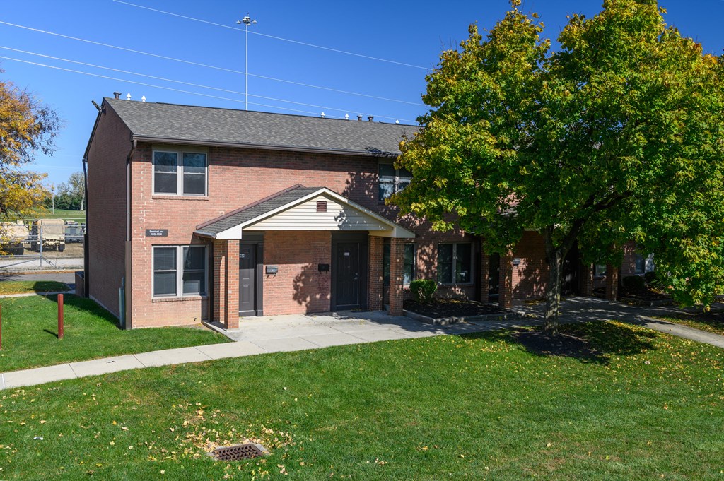 the front of a brick building with a sidewalk and a tree