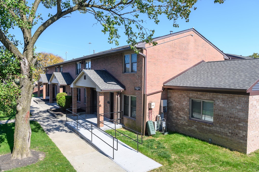 a row of brick apartment buildings with a sidewalk and tree