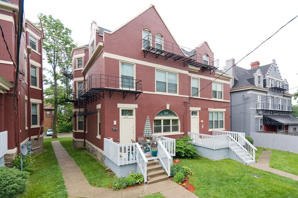 the front of a brick house with a yard and a white fence